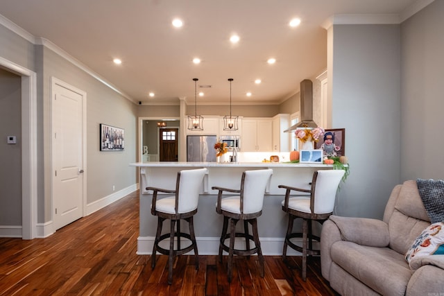 kitchen featuring hanging light fixtures, wall chimney range hood, dark hardwood / wood-style floors, white cabinets, and appliances with stainless steel finishes