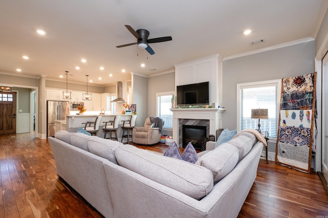 living room with a high end fireplace, dark hardwood / wood-style flooring, ceiling fan, and ornamental molding