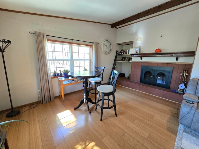 dining room featuring a tile fireplace, light hardwood / wood-style floors, crown molding, and beamed ceiling