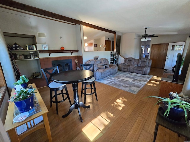 dining space with a tile fireplace, wood-type flooring, lofted ceiling with beams, and ceiling fan