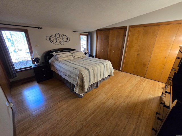 bedroom with a textured ceiling, multiple closets, hardwood / wood-style floors, and lofted ceiling