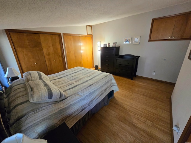 bedroom featuring two closets, lofted ceiling, light hardwood / wood-style floors, and a textured ceiling