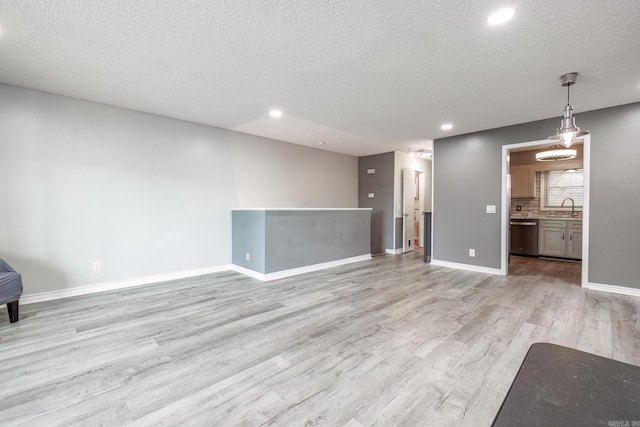 unfurnished living room with a textured ceiling, sink, and light hardwood / wood-style flooring