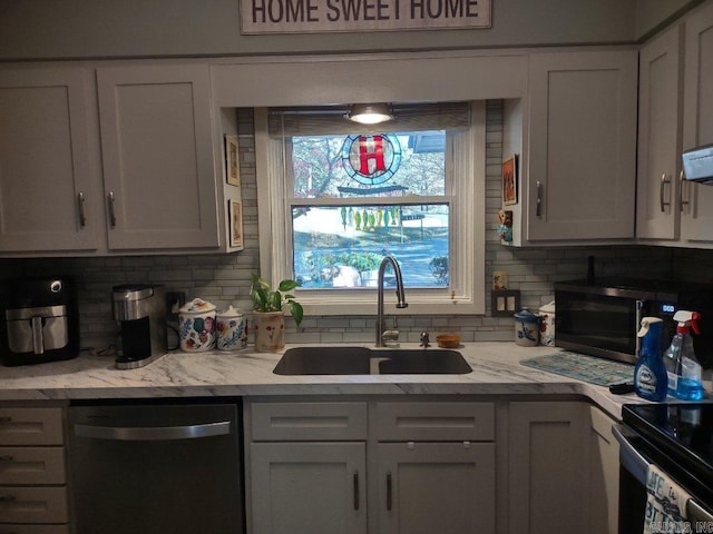 kitchen featuring light stone countertops, white cabinetry, stainless steel dishwasher, and sink