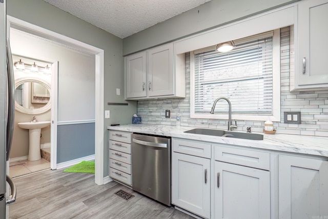 kitchen with white cabinetry, sink, tasteful backsplash, light hardwood / wood-style flooring, and stainless steel dishwasher