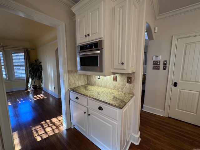 kitchen with dark hardwood / wood-style flooring, light stone counters, ornamental molding, white cabinets, and oven