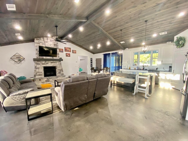 living room featuring concrete flooring, ceiling fan, lofted ceiling with beams, wooden ceiling, and a stone fireplace