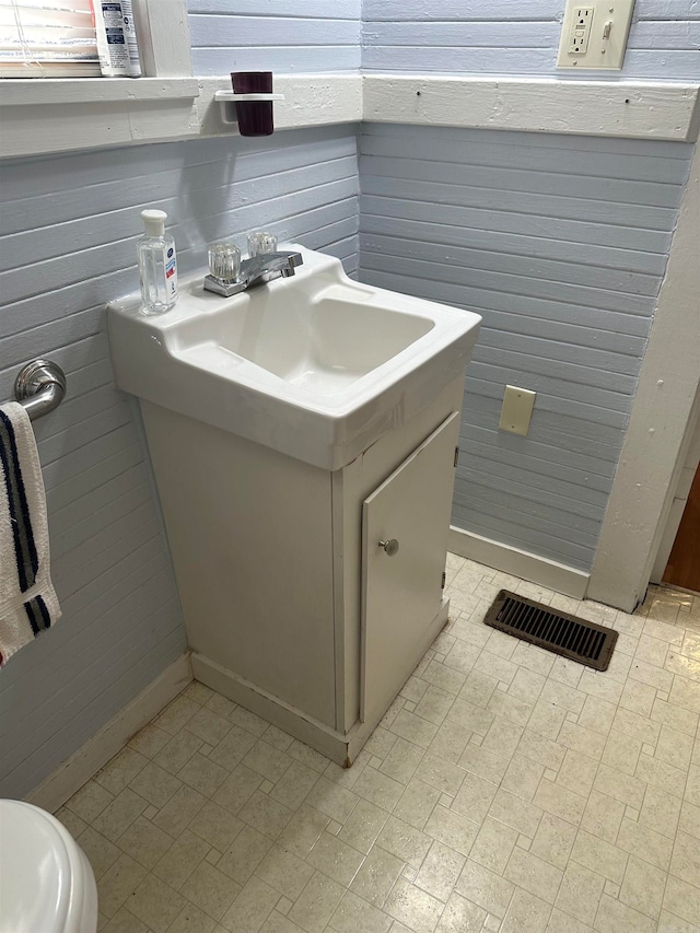 bathroom featuring vanity, wood walls, and toilet