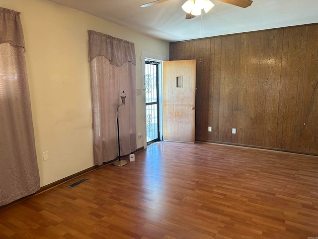 unfurnished room with hardwood / wood-style floors, ceiling fan, and wooden walls