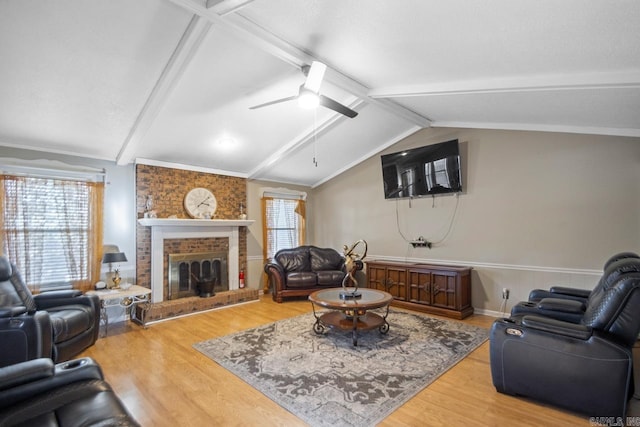 living room with ceiling fan, a brick fireplace, lofted ceiling with beams, crown molding, and wood-type flooring