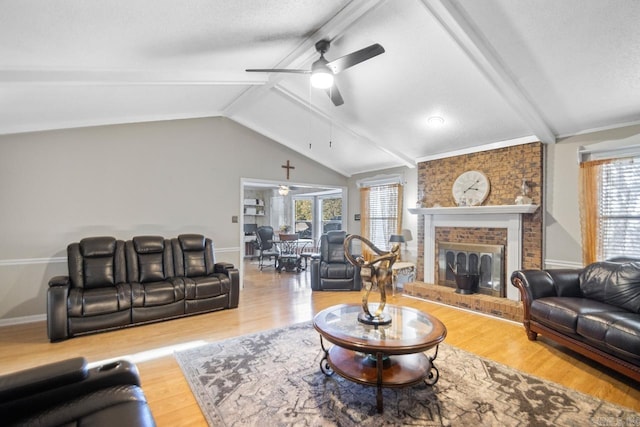 living room featuring vaulted ceiling with beams, ceiling fan, wood-type flooring, and a brick fireplace