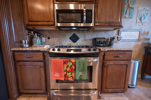 kitchen with light stone counters, light tile patterned floors, backsplash, and appliances with stainless steel finishes