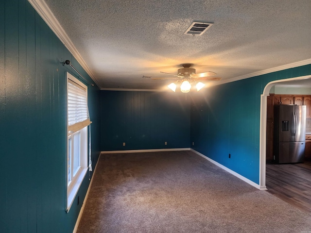 spare room with ceiling fan, dark carpet, ornamental molding, and a textured ceiling