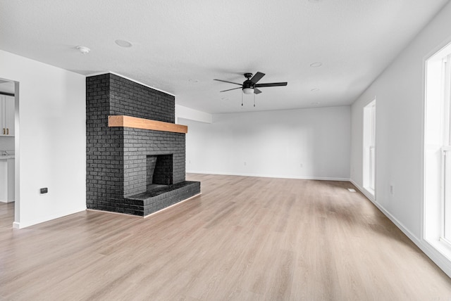 unfurnished living room with ceiling fan, a healthy amount of sunlight, a fireplace, and light hardwood / wood-style flooring