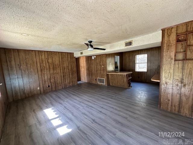 unfurnished living room featuring a textured ceiling, ceiling fan, dark wood-type flooring, and wooden walls