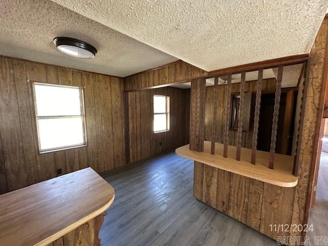 interior space featuring a textured ceiling, wooden walls, a healthy amount of sunlight, and dark hardwood / wood-style floors