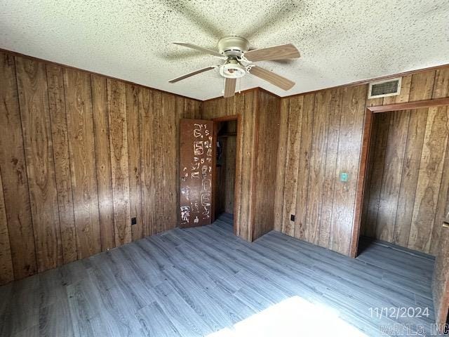 unfurnished bedroom with a textured ceiling, light wood-type flooring, ceiling fan, and wood walls