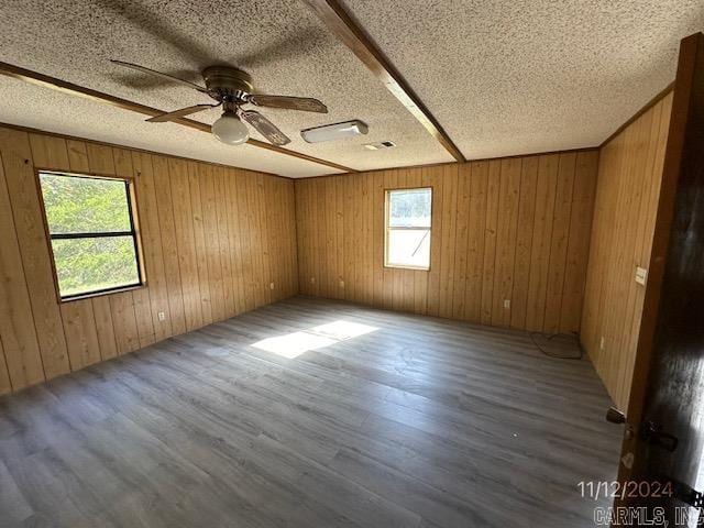 empty room with hardwood / wood-style floors, ceiling fan, a textured ceiling, and wooden walls