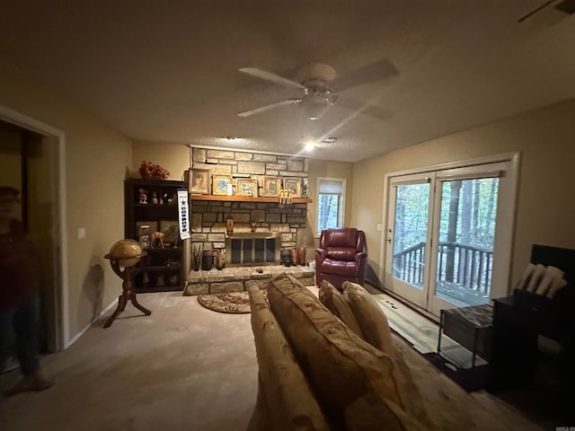 living room featuring a stone fireplace, ceiling fan, and carpet