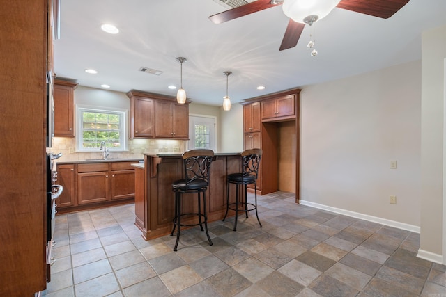 kitchen with a kitchen bar, tasteful backsplash, sink, a kitchen island, and hanging light fixtures