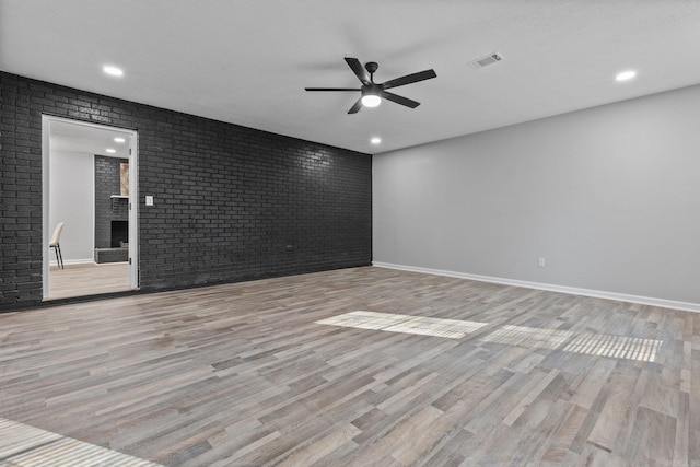 empty room with ceiling fan, a fireplace, brick wall, and light hardwood / wood-style flooring