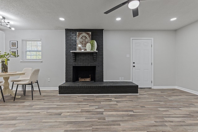 living room featuring a textured ceiling, ceiling fan, a fireplace, and light hardwood / wood-style flooring