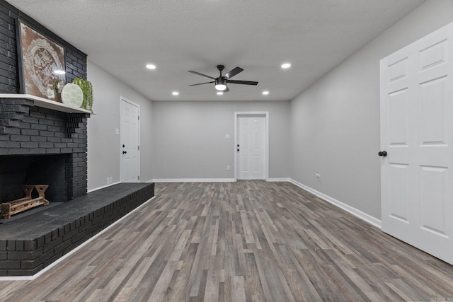 unfurnished living room featuring ceiling fan, hardwood / wood-style floors, a textured ceiling, and a brick fireplace