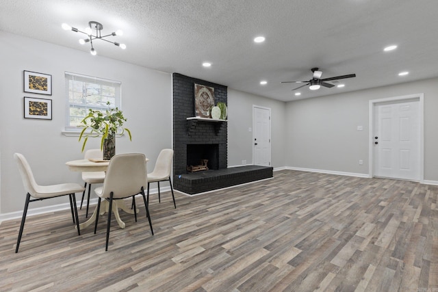 living room with a fireplace, hardwood / wood-style floors, ceiling fan with notable chandelier, and a textured ceiling