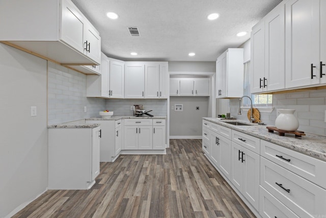 kitchen with white cabinetry, sink, light stone countertops, a textured ceiling, and hardwood / wood-style flooring