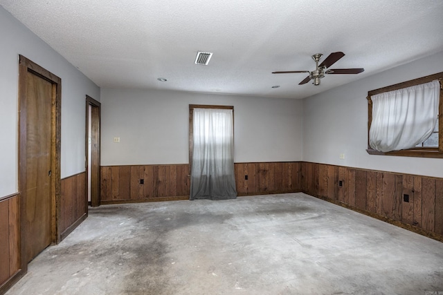 empty room with a textured ceiling, ceiling fan, and wooden walls