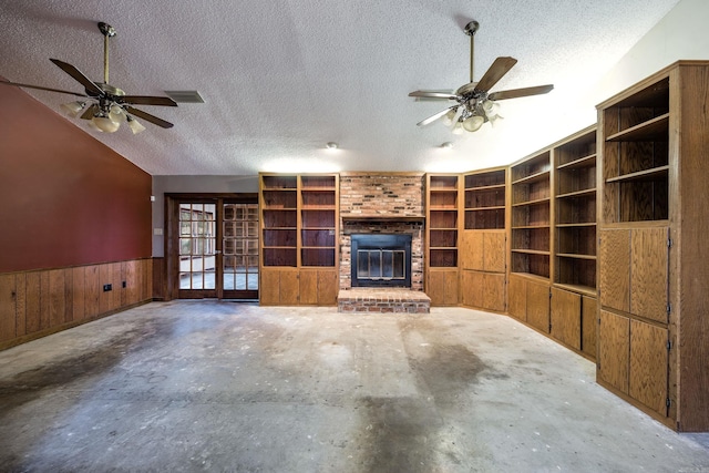 unfurnished living room featuring a brick fireplace, a textured ceiling, ceiling fan, concrete floors, and wood walls