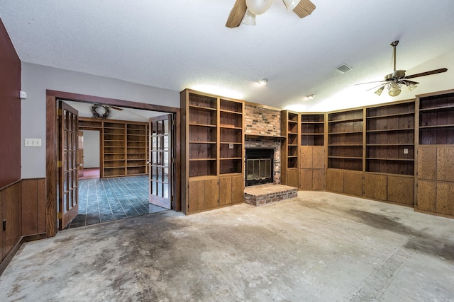 unfurnished living room featuring ceiling fan, wooden walls, a textured ceiling, and a brick fireplace