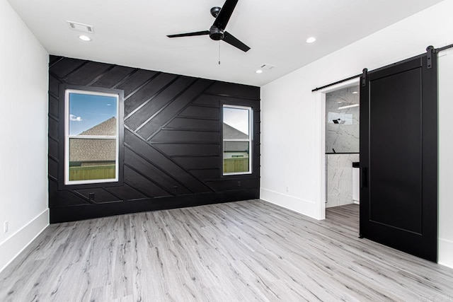 spare room featuring a barn door, light hardwood / wood-style flooring, ceiling fan, and wood walls