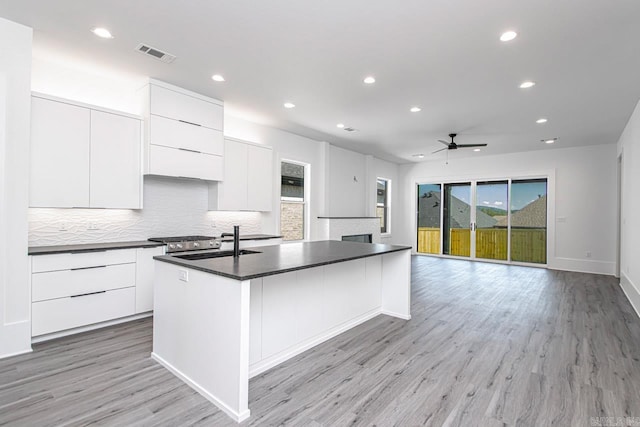 kitchen featuring ceiling fan, sink, a center island with sink, white cabinets, and light wood-type flooring