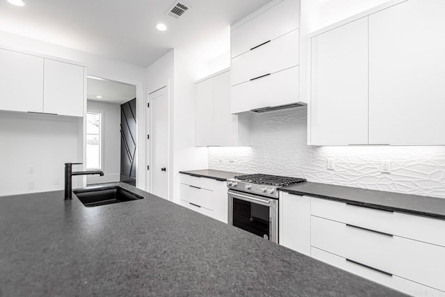 kitchen with tasteful backsplash, white cabinetry, sink, and high end stainless steel range oven