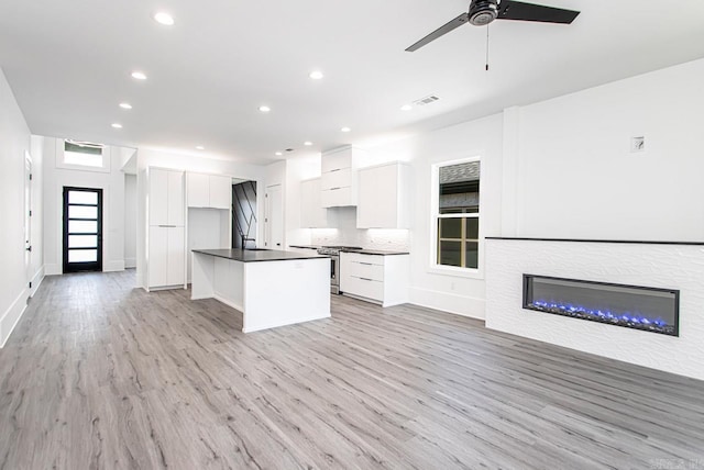 kitchen with stainless steel gas range oven, a center island with sink, ceiling fan, light hardwood / wood-style floors, and white cabinetry