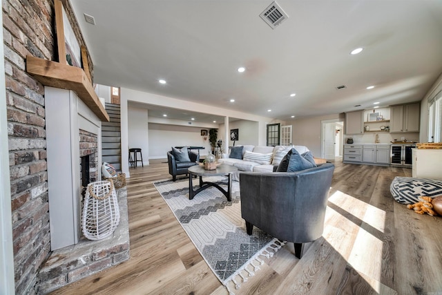 living room featuring wine cooler, sink, light hardwood / wood-style flooring, and a brick fireplace