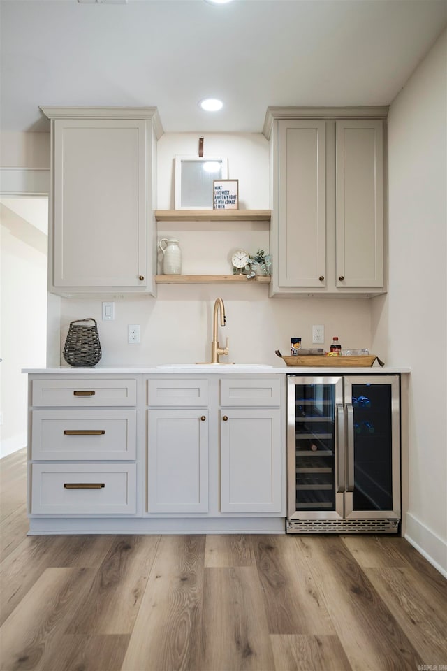 bar with light wood-type flooring, white cabinetry, wine cooler, and sink