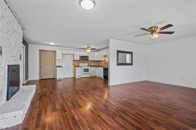 unfurnished living room with a textured ceiling, dark hardwood / wood-style flooring, a stone fireplace, and ceiling fan