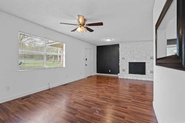 unfurnished living room with a stone fireplace, ceiling fan, dark hardwood / wood-style flooring, and a textured ceiling