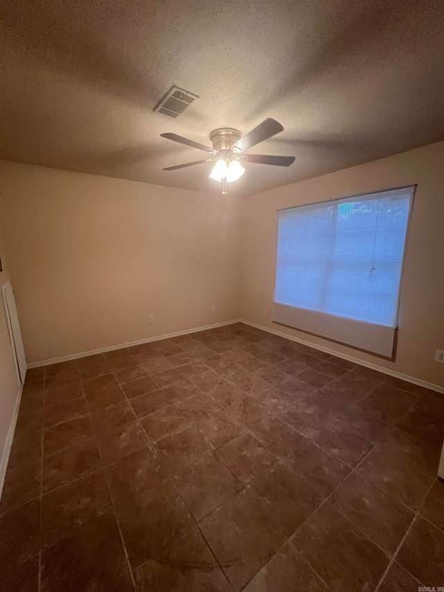 unfurnished room with a textured ceiling, dark tile patterned floors, and ceiling fan