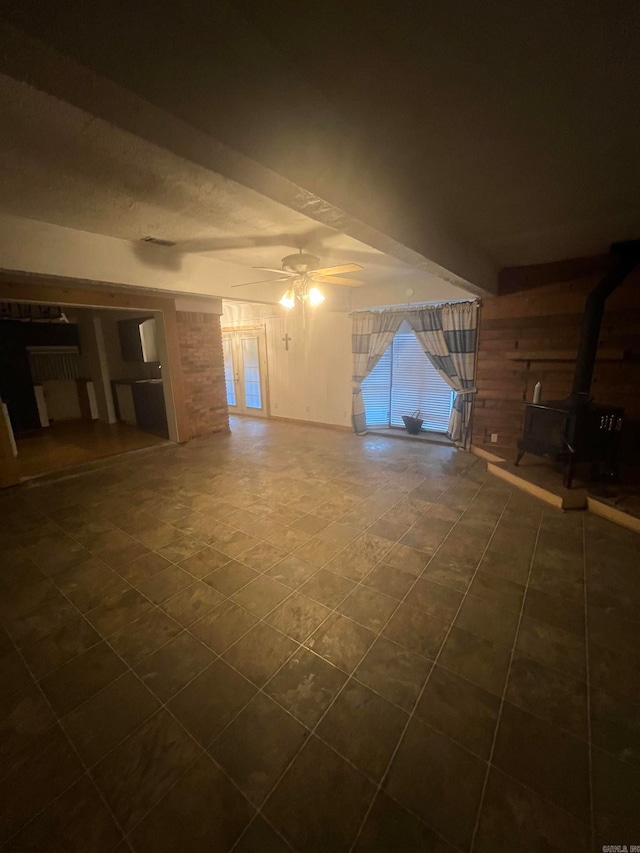 unfurnished living room with ceiling fan, a wood stove, and wooden walls