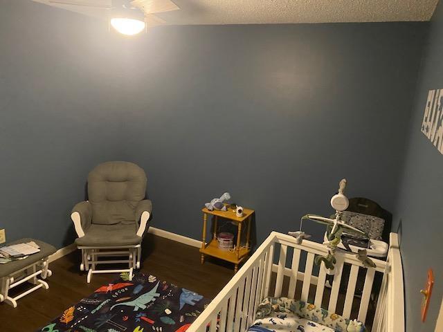 bedroom featuring ceiling fan, hardwood / wood-style floors, a textured ceiling, and a crib