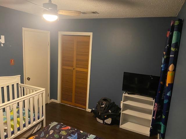 bedroom with dark wood-type flooring, a textured ceiling, a closet, ceiling fan, and a crib