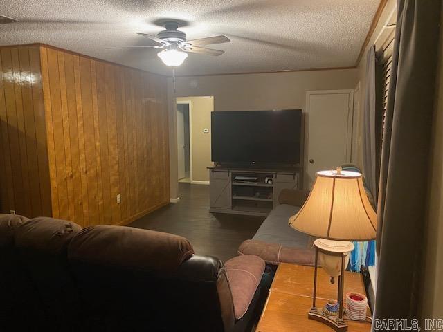 living room with ceiling fan, wooden walls, and a textured ceiling