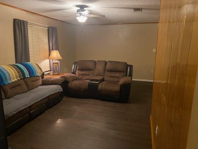 living room with dark wood-type flooring, ceiling fan, crown molding, and a textured ceiling