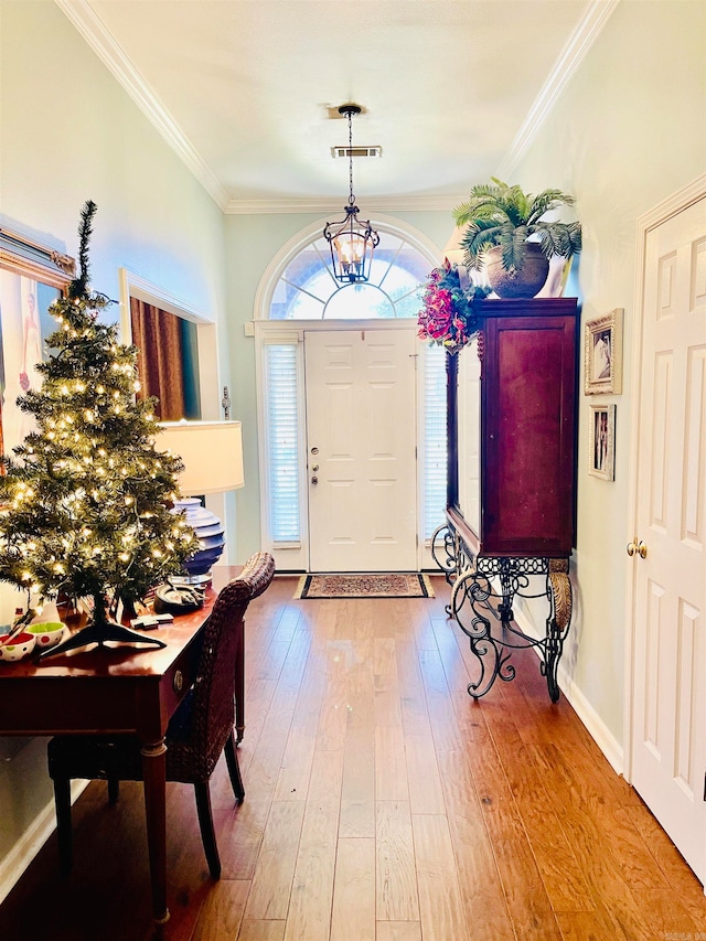 entryway with wood-type flooring, crown molding, and a chandelier