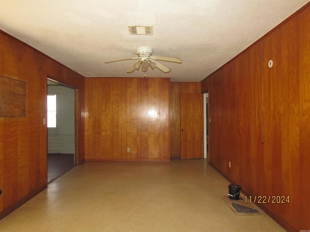 spare room featuring ceiling fan, wooden walls, and a textured ceiling