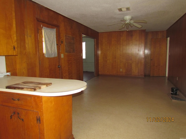 kitchen with ceiling fan, wood walls, and a textured ceiling