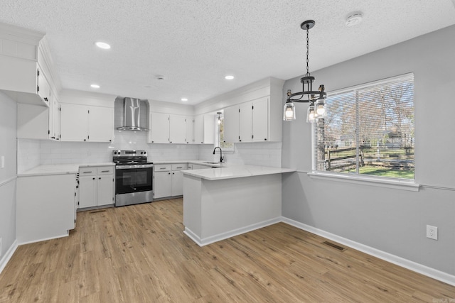 kitchen with stainless steel range with electric stovetop, wall chimney exhaust hood, white cabinets, and decorative light fixtures